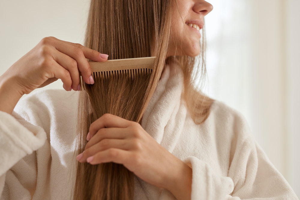 Smiling woman in robe combing long healthy hair, showing positive results of early PRP hair restoration treatment