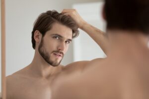 Shirtless man examining thinning hair in mirror before PRP hair restoration treatment for hair loss