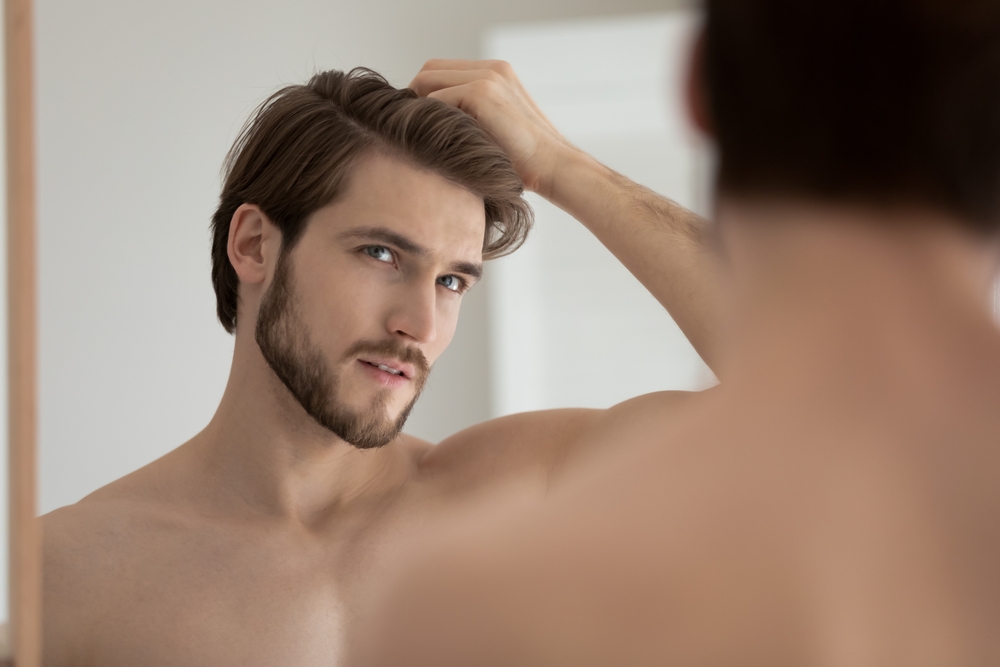 Shirtless man examining thinning hair in mirror before PRP hair restoration treatment for hair loss