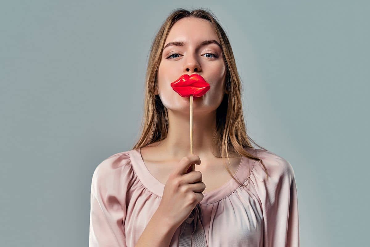 Woman holding red lips prop symbolizing cosmetic filler issues and the rise of poorly performed aesthetic treatments.