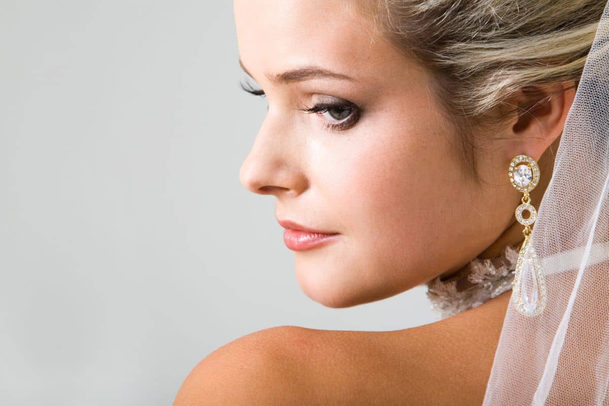 Elegant woman with veil and statement earrings looking over shoulder, ideal rhinoplasty timing before wedding