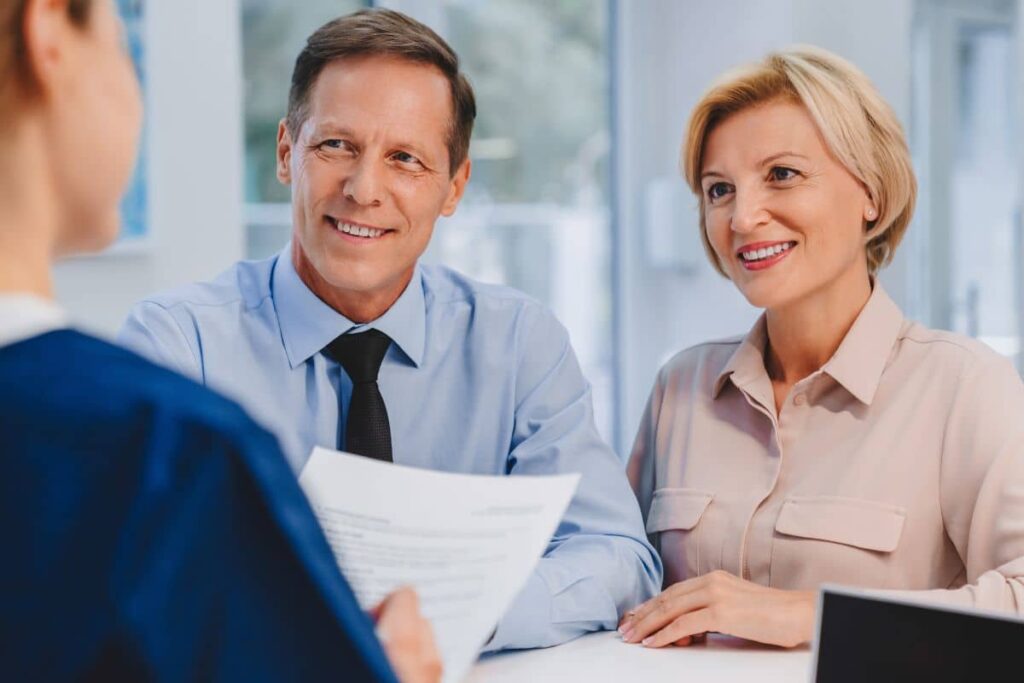 Smiling couple discussing nose surgery financing options with a medical professional at a clinic.