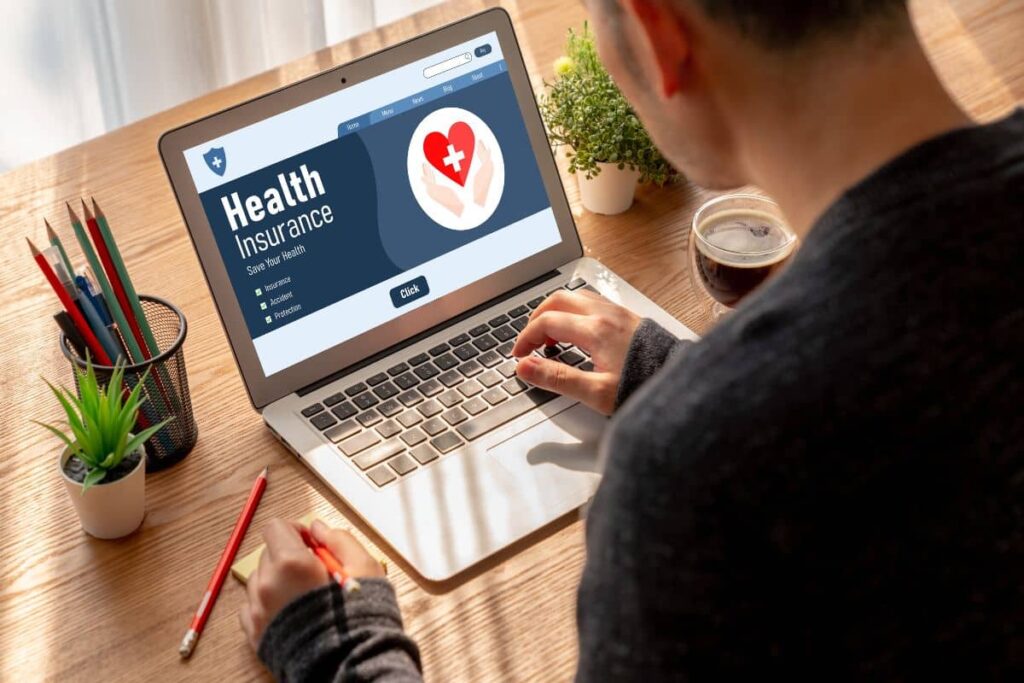 ndividual reviewing health insurance information on laptop with coffee and notepad, focusing on cost-related terms.