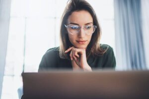 Young woman looking at laptop screen while researching rhinoplasty surgery options and international clinic safety.