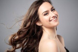 Woman smiling confidently with flowing hair after hybrid rhinoplasty showing natural and balanced nose refinement.