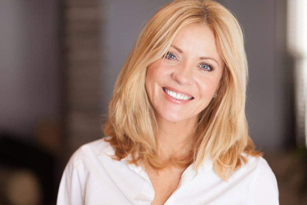 Middle-aged woman with smooth skin and bright smile after facial rejuvenation, possibly from facelift or filler treatments.