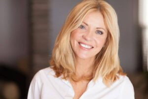 Middle-aged woman with smooth skin and bright smile after facial rejuvenation, possibly from facelift or filler treatments.