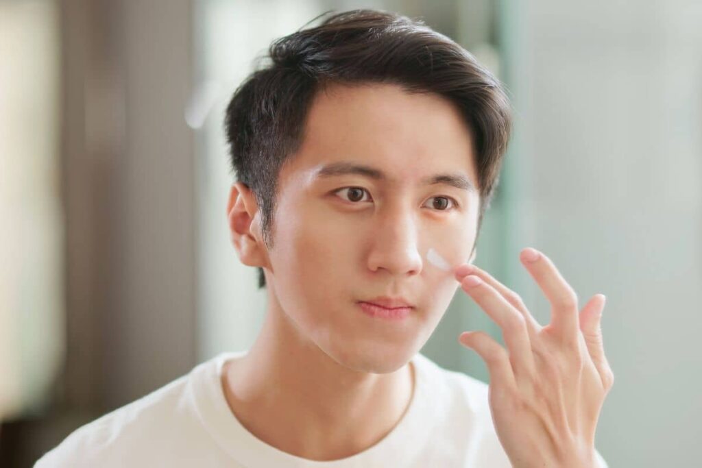 Young man applying sunscreen to his face as part of daily skincare routine to manage hyperpigmentation effectively.
