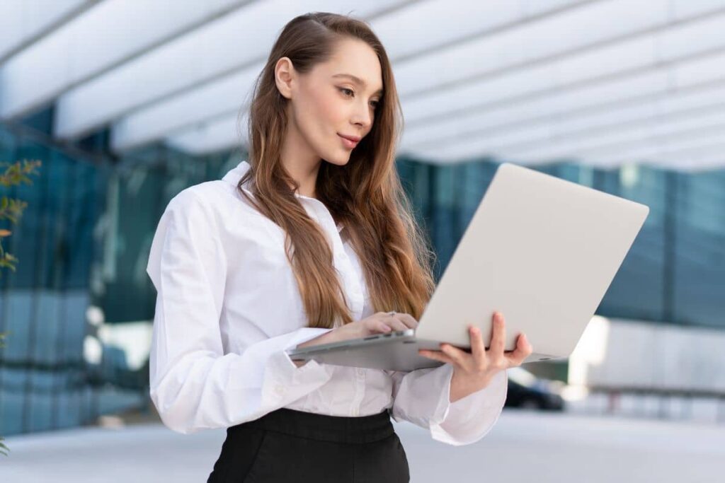 Professional woman with refined facial features using a laptop, representing natural-looking rhinoplasty for balance and confidence