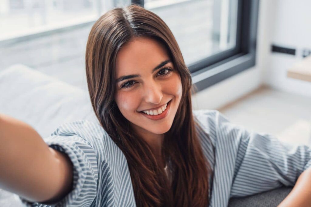 Young woman smiling confidently indoors, representing the prejuvenation trend in non-surgical cosmetic treatments.