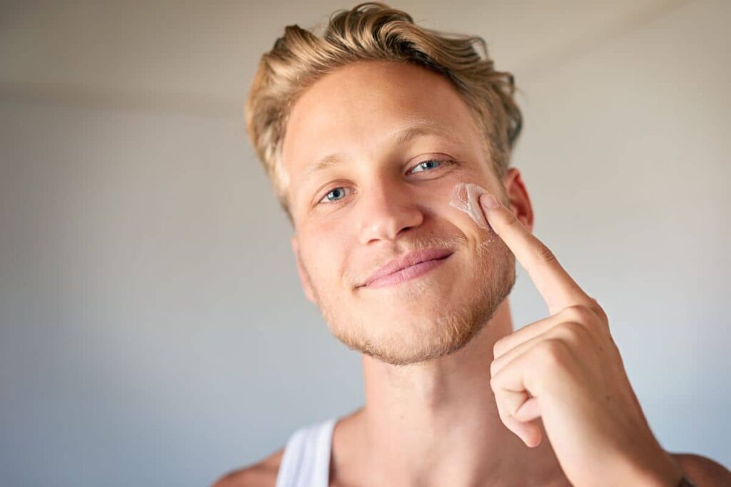 miling man applying cream to face, highlighting the importance of medical-grade skincare in prejuvenation routines.