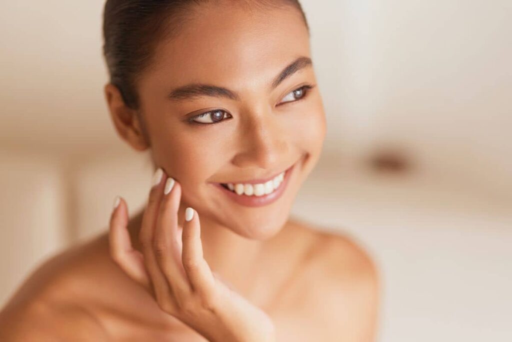 Smiling woman gently touching her cheek, symbolizing a holistic prejuvenation treatment plan for youthful, healthy skin.