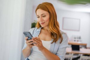 Young woman browsing phone, reflecting rise of TikTok-driven trends in non-invasive and natural cosmetic enhancements.