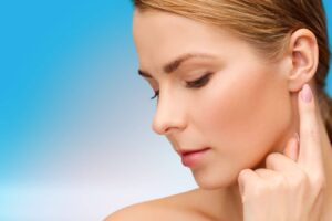 Woman gently touching her earlobe, illustrating healing and recovery after earlobe repair surgery for torn or stretched piercings.