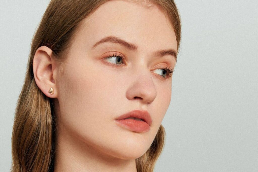 Woman wearing earrings showing healed earlobe after repair surgery and readiness for safe ear re-piercing.