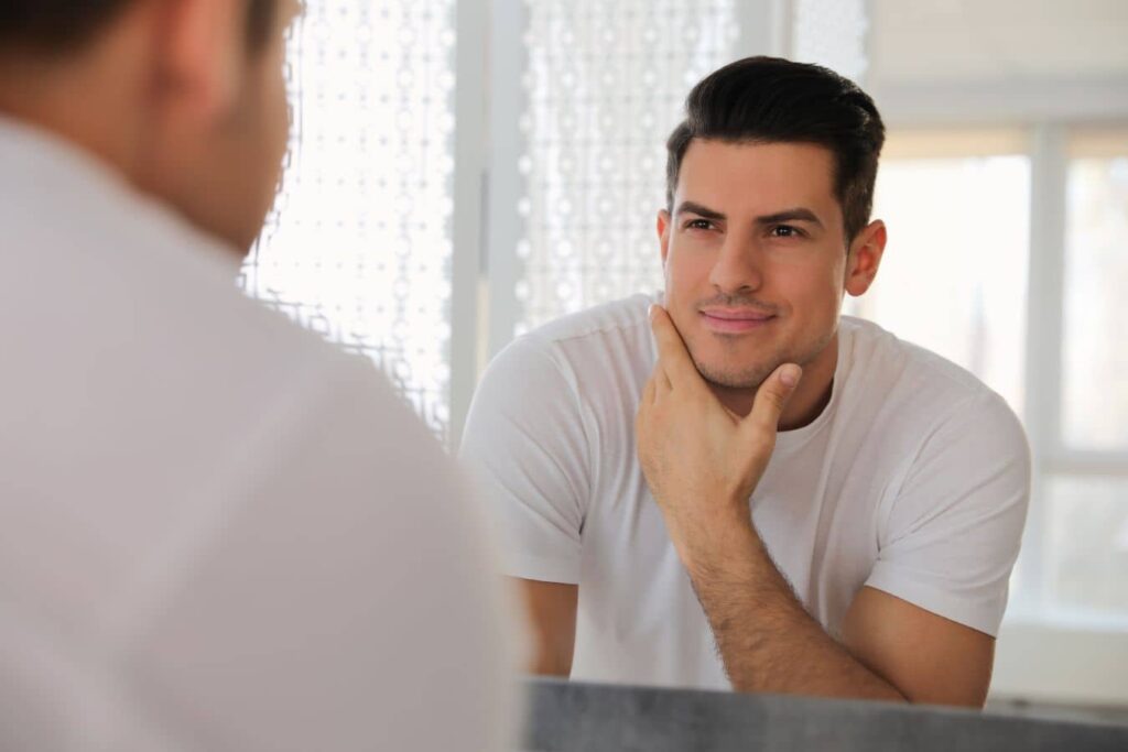 Man examining skin in mirror, representing natural PRF results and gradual collagen improvement over time.