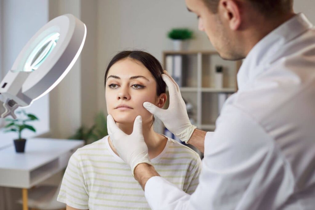 Practitioner assessing woman’s face during dermal filler reversal consultation, focusing on natural balance and facial harmony