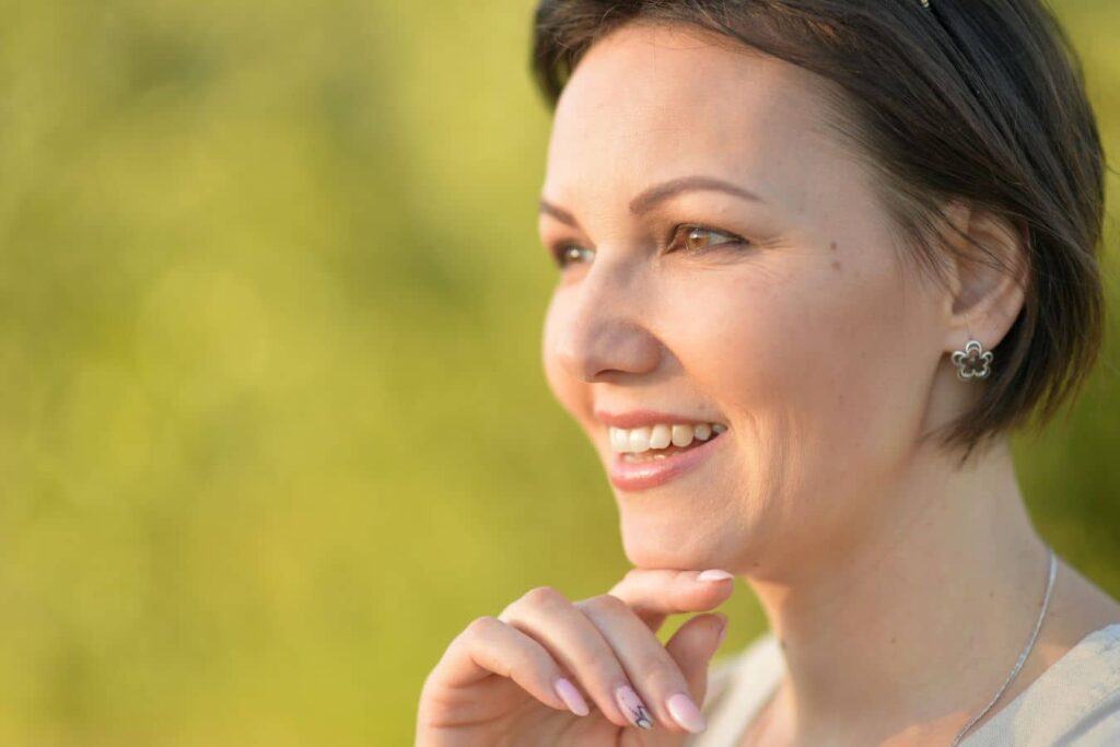 Woman smiling outdoors showing natural appearance during deep plane facelift recovery timeline.