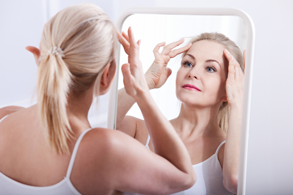 Woman examining facial contours in mirror, reflecting growing demand for deep plane facelift surgery in 2026.