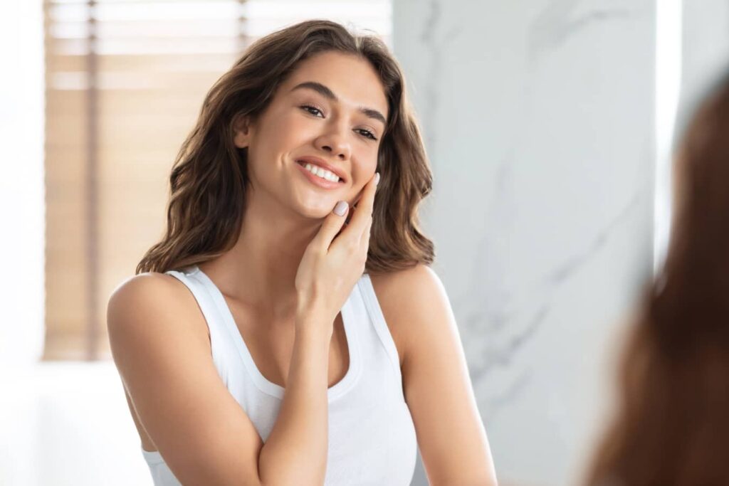 Young woman touching her face, reflecting the trend toward deep plane facelift and natural facial rejuvenation over fillers.