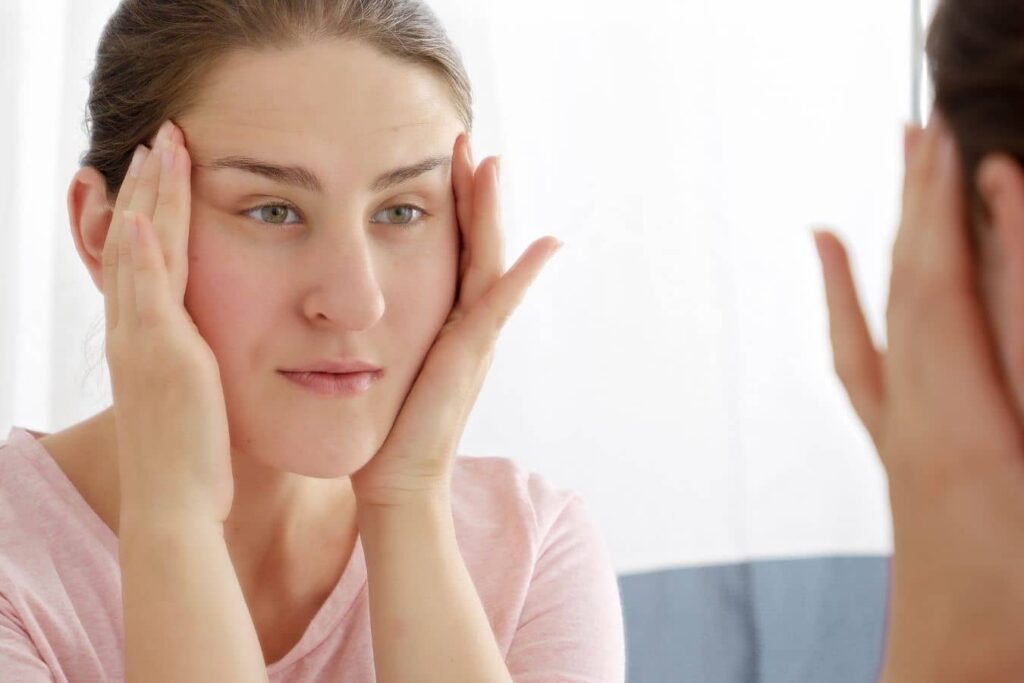 Woman examining her face in a mirror, showing concerns about skin tightening and natural facelift results.