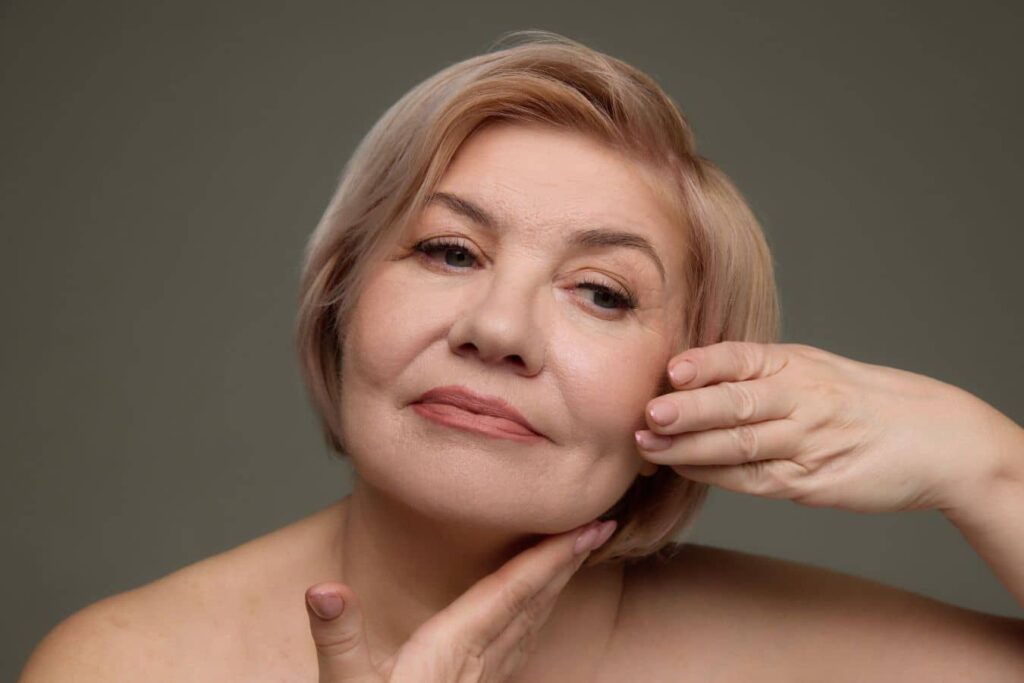 Mature woman touching her face, representing facelift recovery refinement as tissues soften and settle.