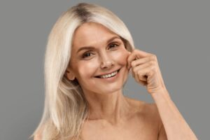Mature woman with a warm smile illustrating facial aging, jowls, and hollowing anatomy.