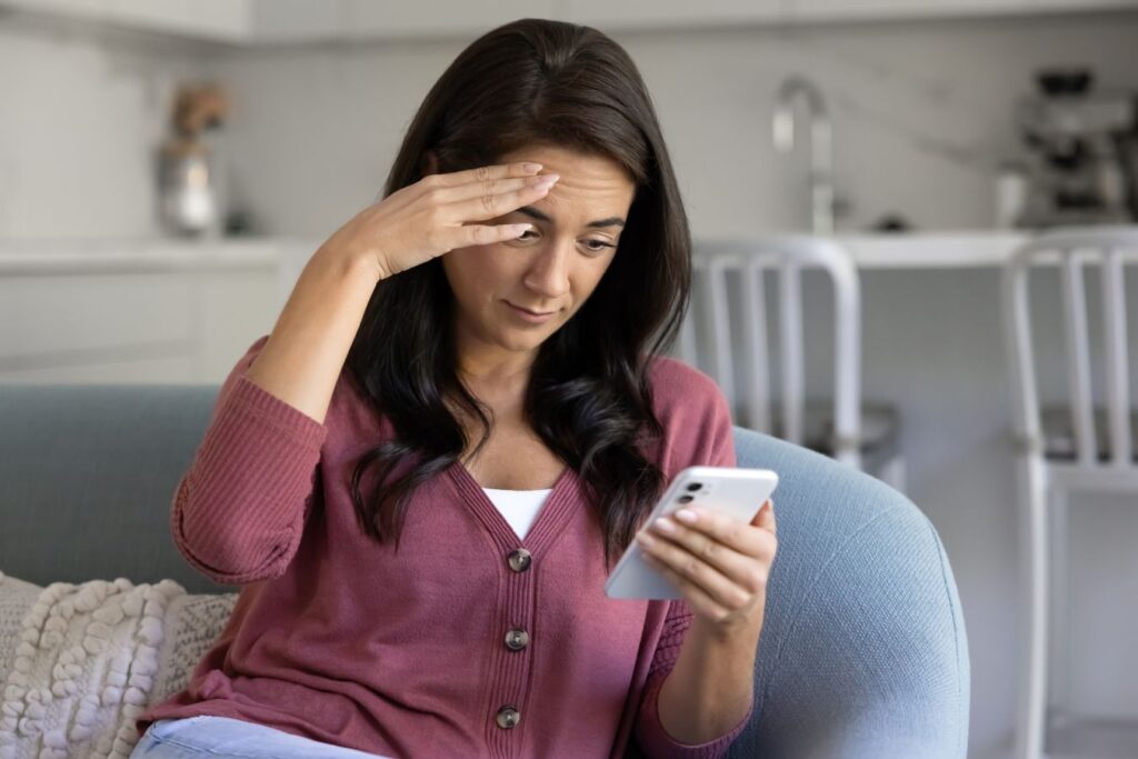 Concerned woman viewing her smartphone, showing how Zoom and social media increase awareness of facial aging.