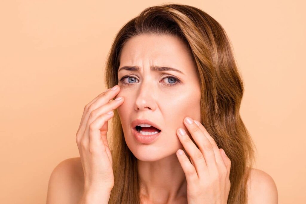 Concerned woman touching her face, illustrating unnatural facelift results and common surgical mistakes discussed in facelift surgery.
