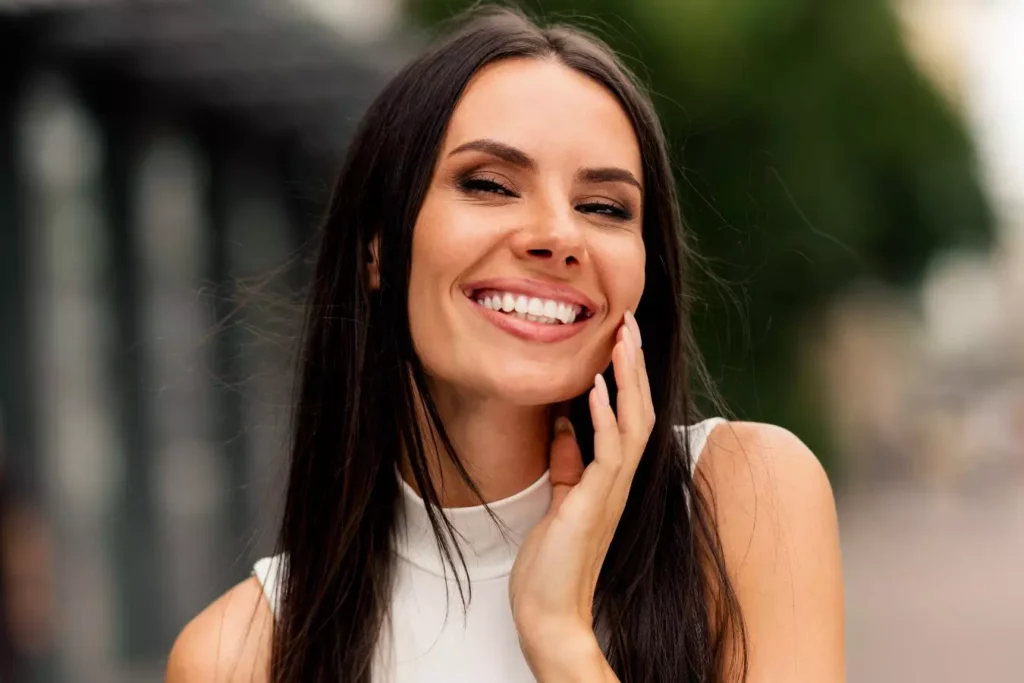 Smiling woman touching her cheek, representing facial rejuvenation.