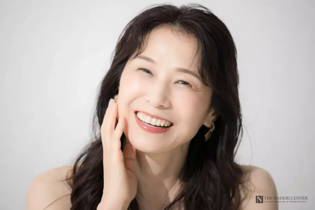 Smiling woman touching her cheek, illustrating deep plane facelift rejuvenation.