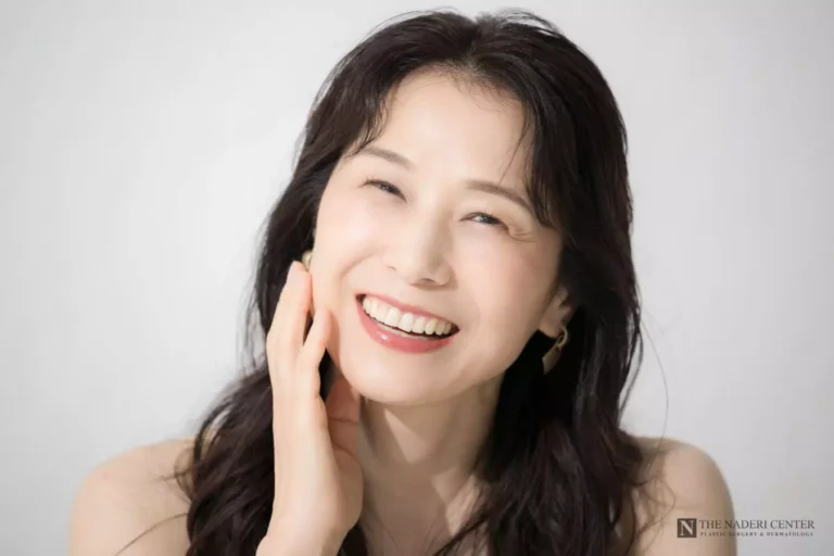 Smiling woman touching her cheek, illustrating deep plane facelift rejuvenation.