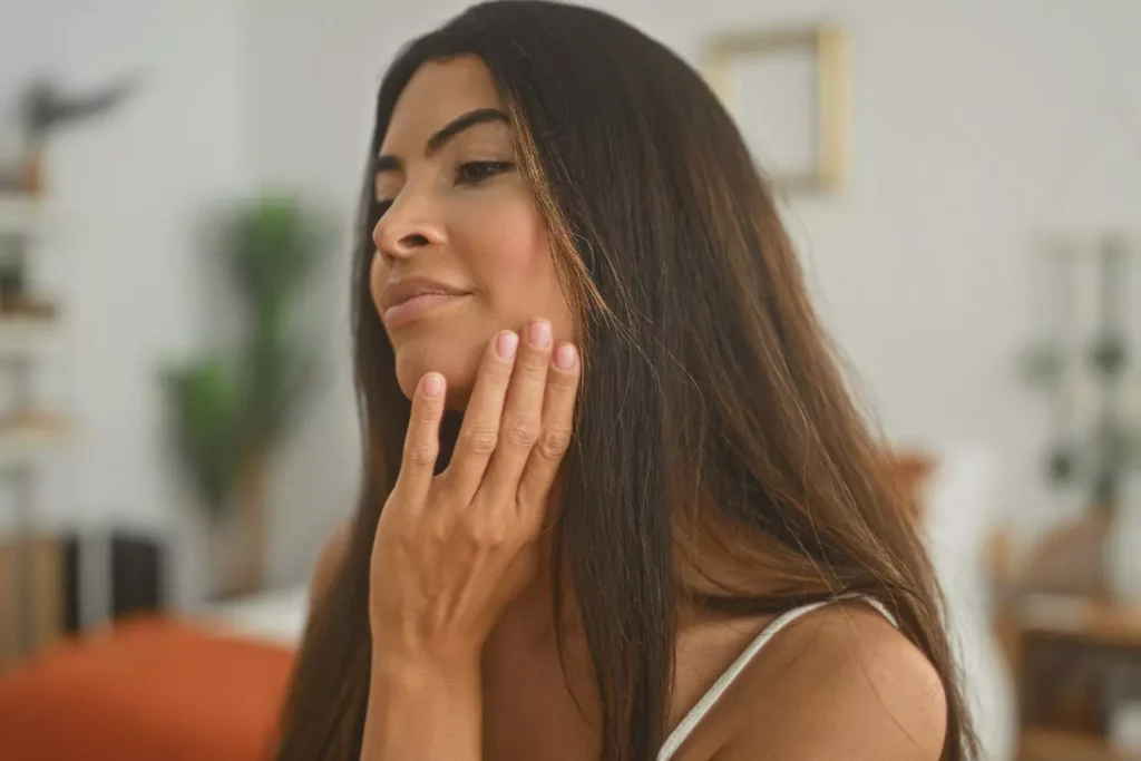Woman gently touching her jawline, illustrating the healing process and recovery timeline after deep plane facelift surgery.