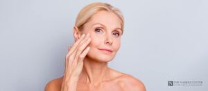Woman with smooth, rested-looking eyes touching her cheek, representing upper eyelid surgery at The Naderi Center in Reston and Chevy Chase